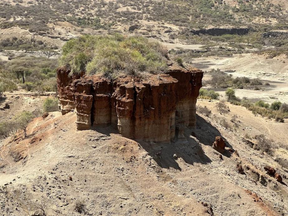 Red layered rock formation rising from Olduvai Gorge